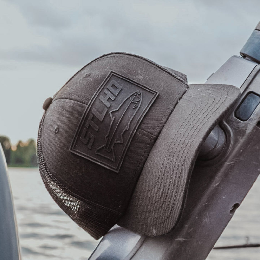 All-black STLHD Blackout Trucker hat with black logo on the front panel and black mesh back.