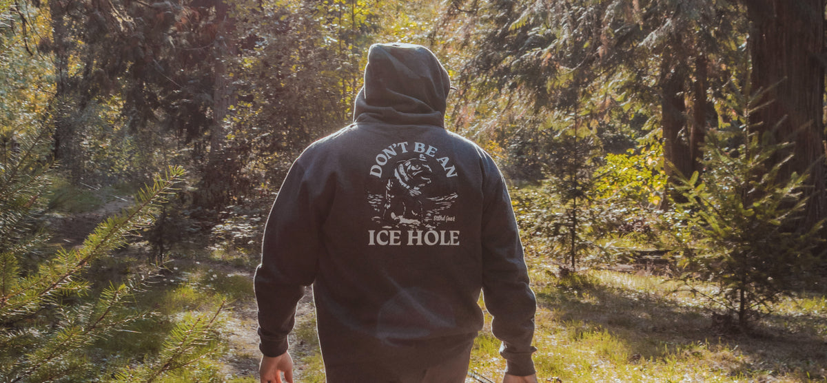 A person viewed from behind wearing a dark hoodie with a white graphic and the text 'DON'T BE AN ICE HOLE' on the back, standing in a sunlit forest path.