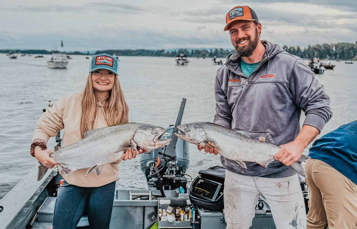 2 people wearing STLHD hats and carrying 2 fishes